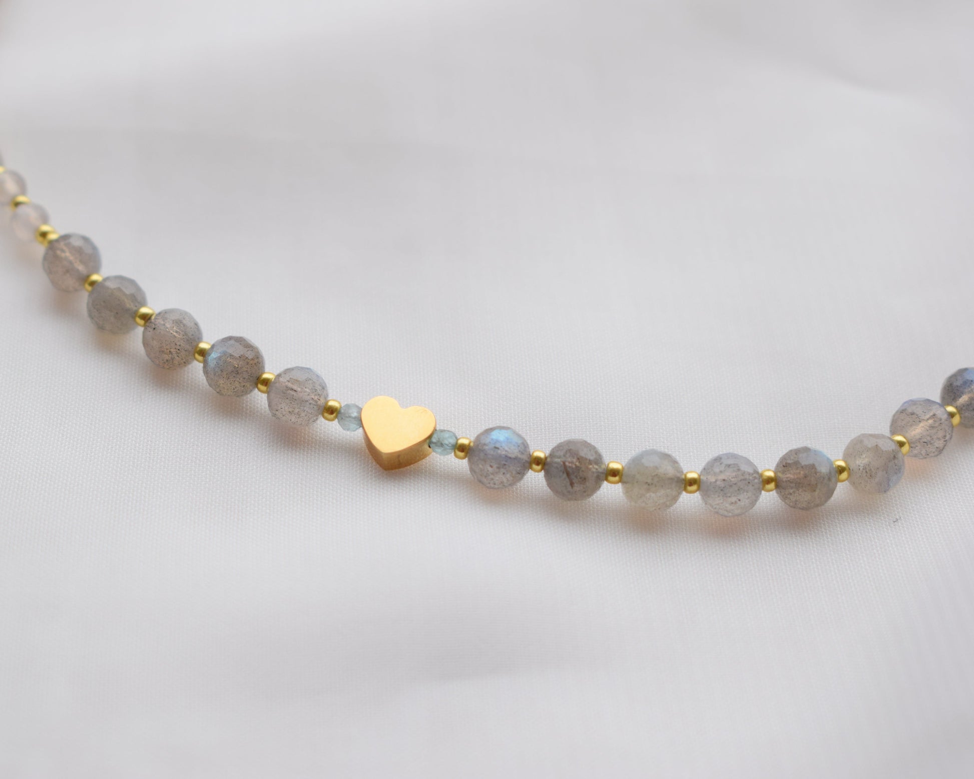 Necklace with Labradorite beads and a gold heart charm on a light background